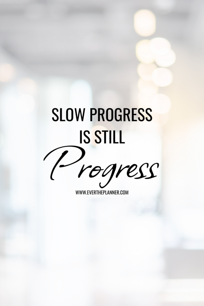 Quote-style graphic with the phrase “Slow Progress Is Still Progress” over a softly blurred white background with warm lights.